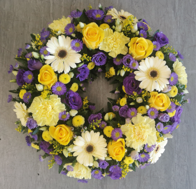 Wreath SYM-316 - A beautiful classic wreath arranged using purple and white flowers and finished with fine foliage.
