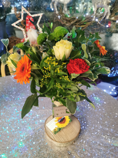 A rustic Xmas - A seasonal mix of flowers in a jam jar on a log slice